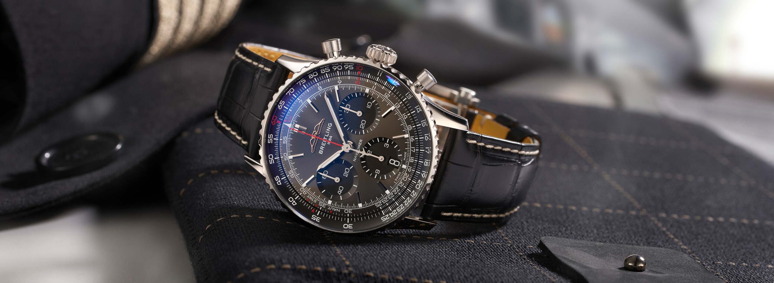 uhrenikonen-breitling-navitimer-intro-2732_1000 Breitling Navitimer liegend auf einem Tisch. Im Hintergrund der Ärmel einer Pilotenuniform.