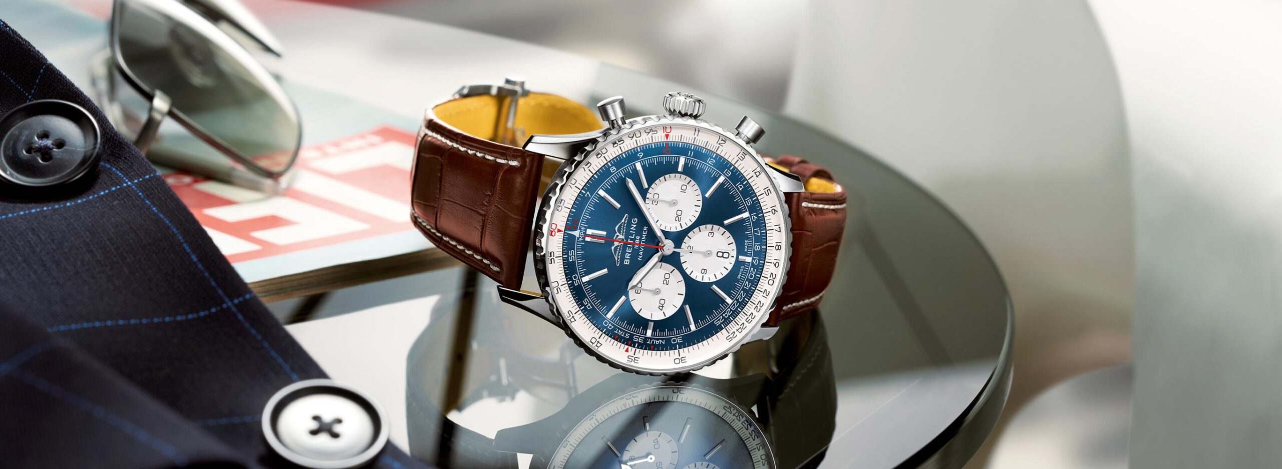 Uhrenikonen und bekannte Uhrenkollektionen -Breitling Navitimer mit blauem Zifferblatt, weißen Totalisatoren und braunem Lederarmband auf einem Glastisch.